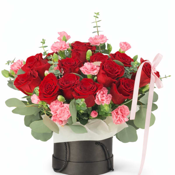Red roses and pink carnations in a black hatbox with a pink ribbon
