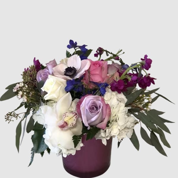 Mixed bouquet of roses, hydrangeas, and orchids in a purple vase