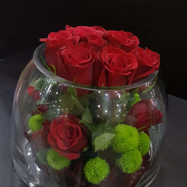 Red roses and green pom-pom flowers in a clear glass bowl