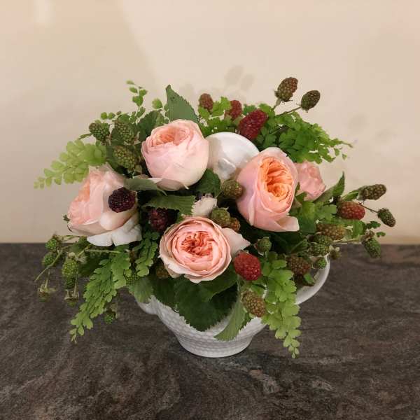 Pink roses arranged in a white teacup vase with green berries and foliage
