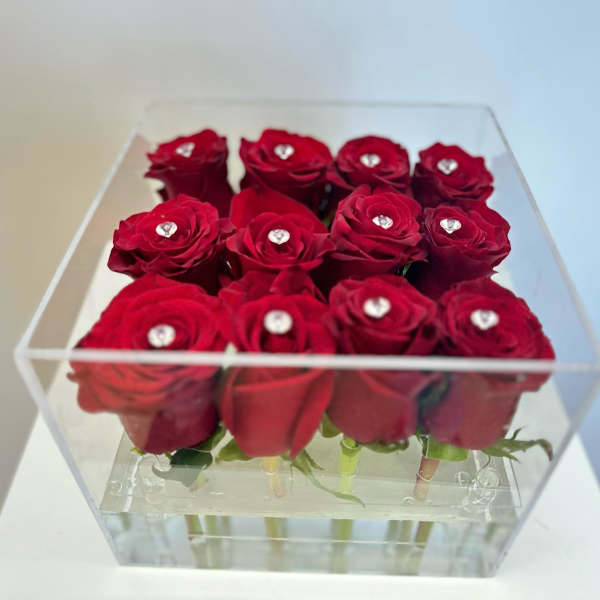 Red roses arranged in a clear acrylic box with small gem accents