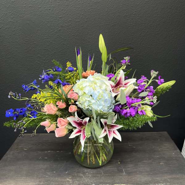 Mixed bouquet in a glass vase with lilies, hydrangea, roses, and purple blooms