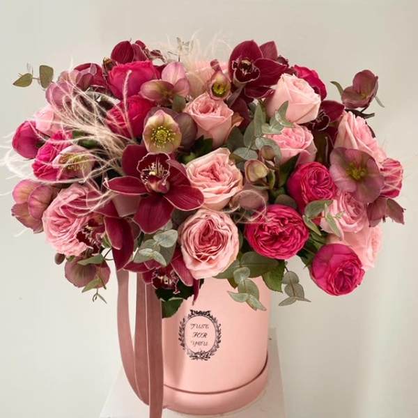 Pink and burgundy flower arrangement in a round hatbox with ribbon