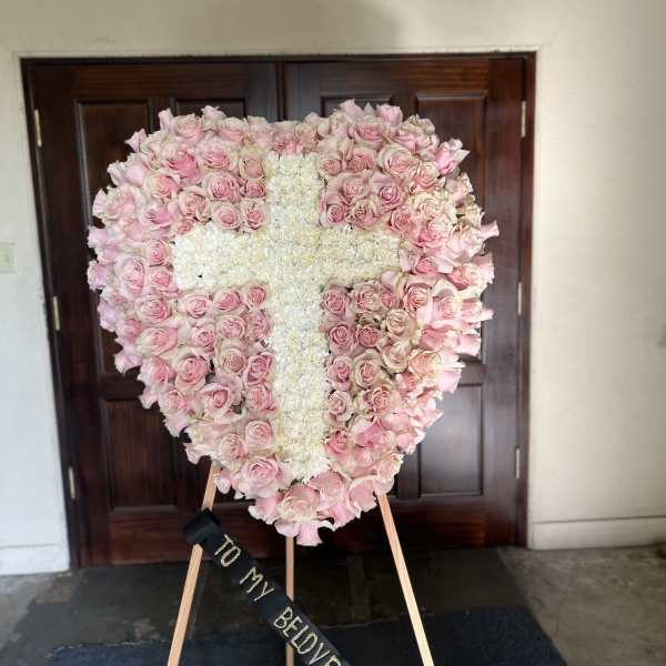 Heart-shaped pink rose wreath with a white floral cross on an easel
