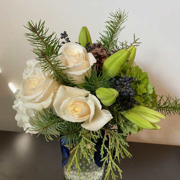 White roses and green lilies in a glass vase with pine accents