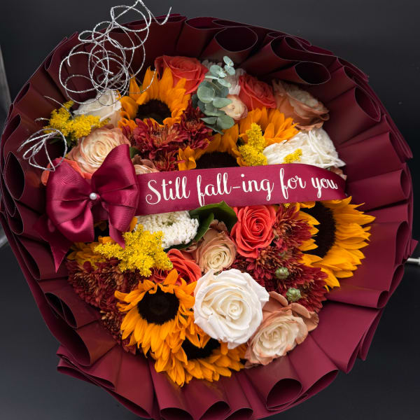 Bouquet of sunflowers and roses wrapped in burgundy paper with a ribbon