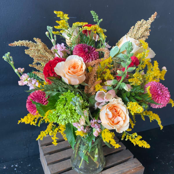 Mixed bouquet of peach roses, pink blooms, and yellow filler in a glass vase