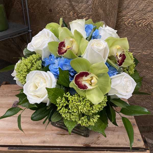 Bouquet of white roses, green orchids, and blue hydrangeas in a glass vase