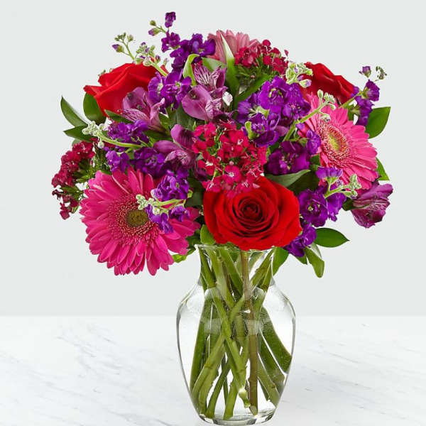 Bouquet of red roses, pink gerbera daisies, and purple flowers in a glass vase