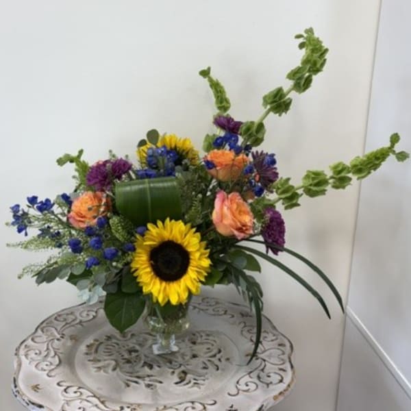 Colorful bouquet with sunflowers, roses, and blue flowers in a glass vase