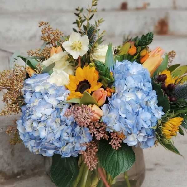 Mixed bouquet with blue hydrangeas, sunflowers, and tulips in a glass vase