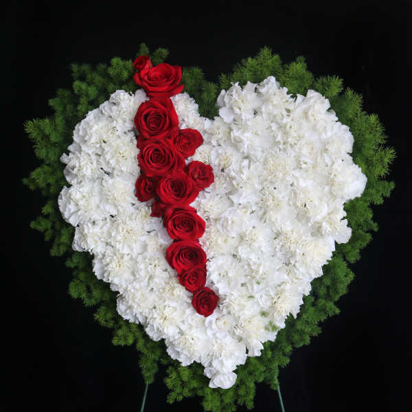 Heart-shaped floral spray of white carnations with red roses on a stand