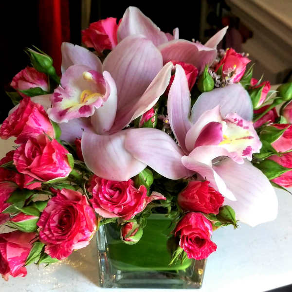 Pink roses and pale lilies arranged in a square glass vase