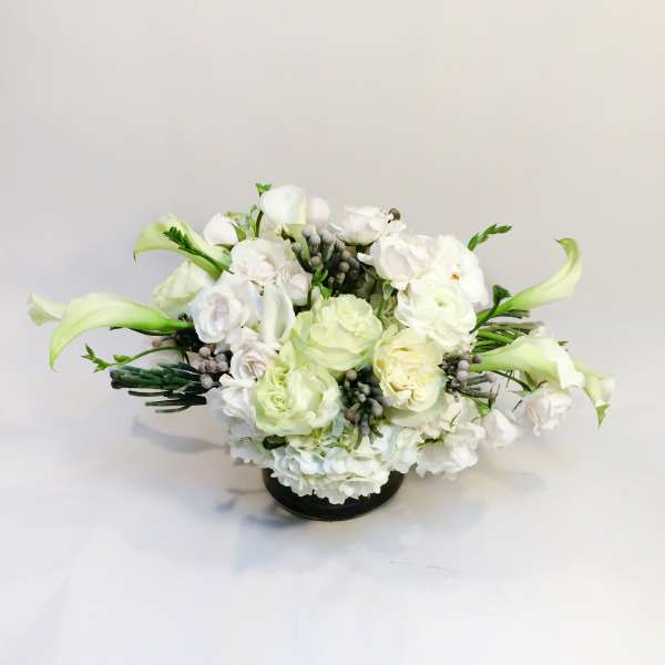 White floral arrangement with pale green calla lilies in a low black vase