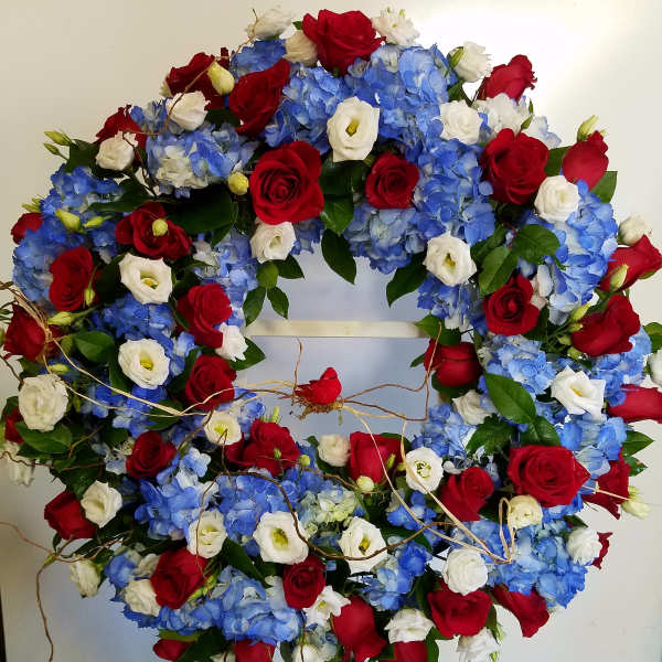 Circular wreath of red roses, blue hydrangeas, and white blooms