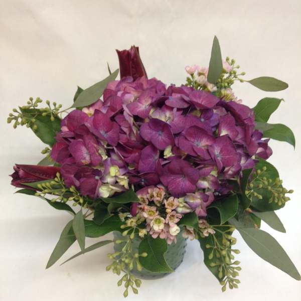 Purple hydrangea bouquet with greenery in a small vase