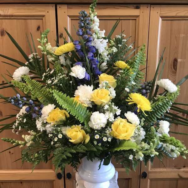 Large floral arrangement with yellow roses, white blooms, and blue flowers in a white vase