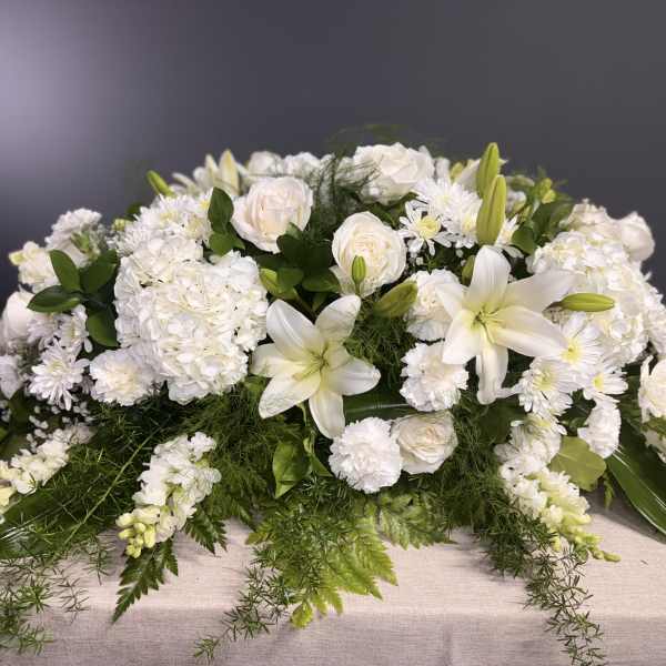White floral casket spray with lilies, roses, and chrysanthemums