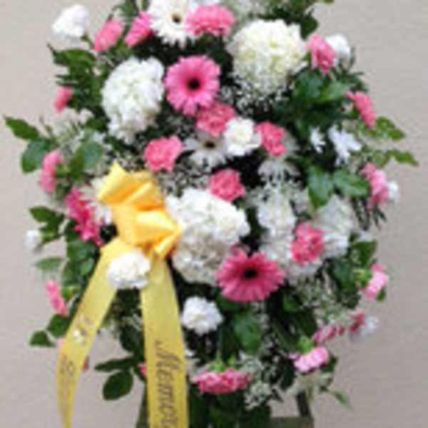 Standing floral spray of pink and white flowers with a yellow ribbon