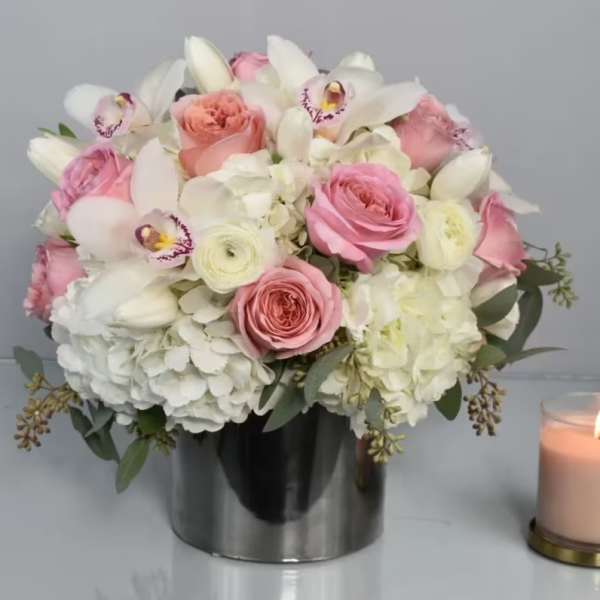 Pink and white bouquet in a silver vase beside a lit candle