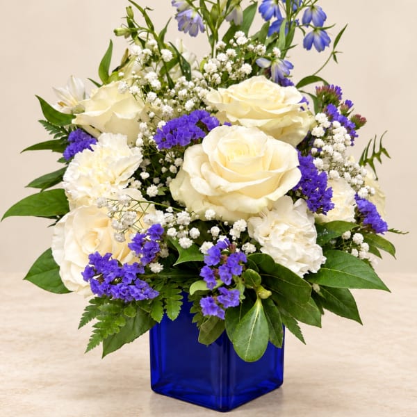 White roses and purple flowers in a blue glass vase