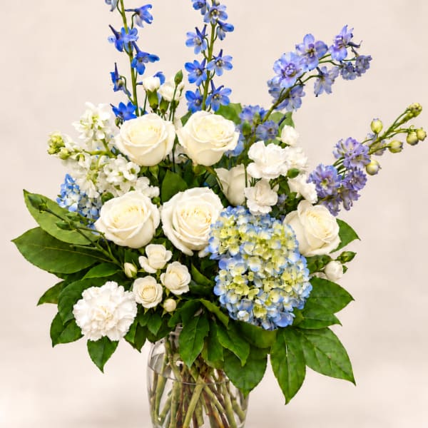 White roses and blue flowers arranged in a clear glass vase