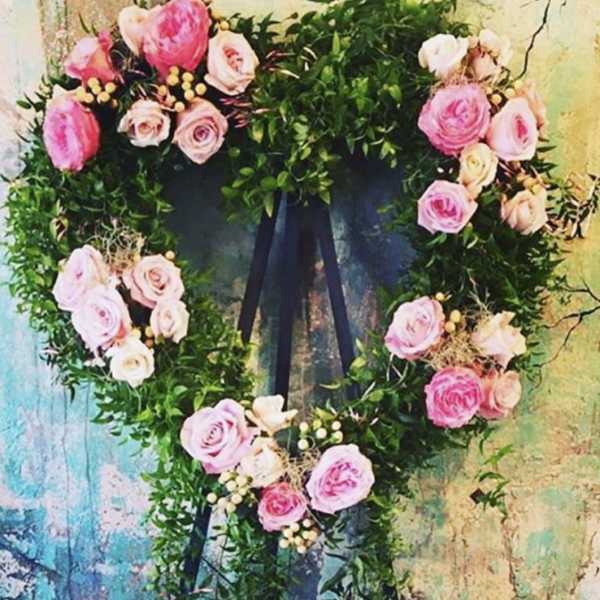 Heart-shaped floral wreath with pink roses and greenery on a dark ribbon
