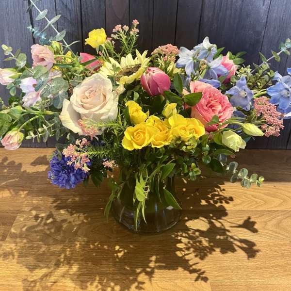 Mixed bouquet in a glass vase with roses, tulips, and blue flowers