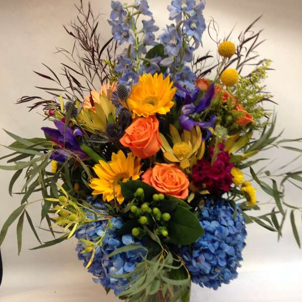 Colorful mixed bouquet in a clear glass vase with blue hydrangeas and orange roses
