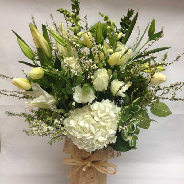 White floral arrangement with lilies and hydrangea in a burlap-wrapped vase