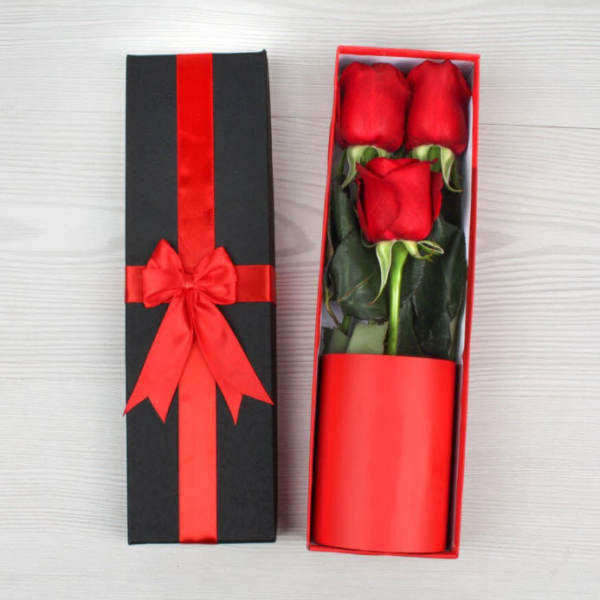 Three red roses in a black gift box with a red ribbon
