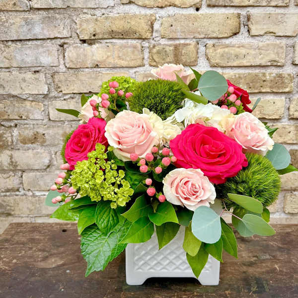 Pink and white roses in a white square vase with greenery