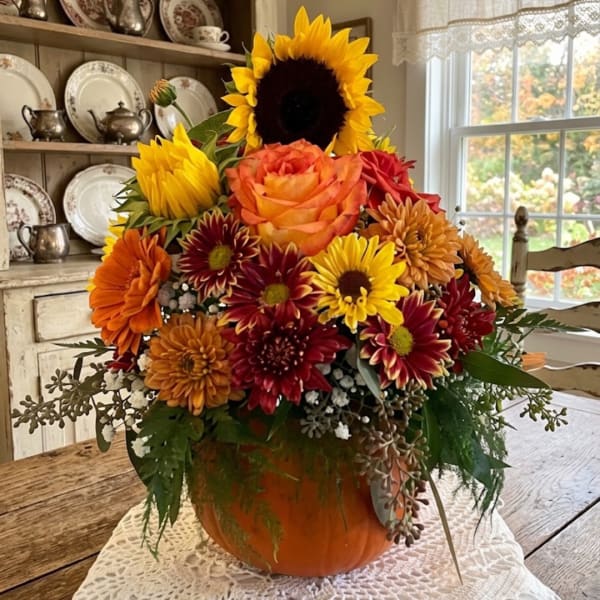 Autumn floral arrangement in a pumpkin-shaped container with sunflowers, roses, and mums