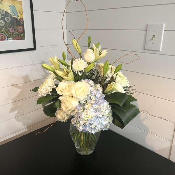 Cream roses, lilies, and blue hydrangeas in a glass vase