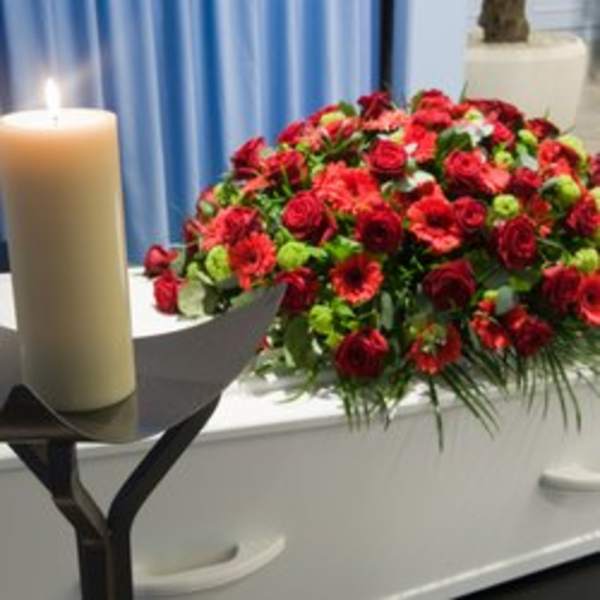 Red floral casket spray with a lit candle beside it