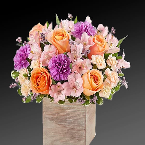 Bouquet of peach roses, purple carnations, and pink flowers in a wooden cube vase