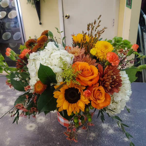 Mixed bouquet with orange roses, sunflowers, white hydrangeas, and chrysanthemums in a checkered container