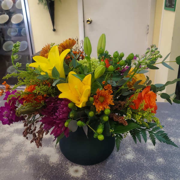 Colorful mixed flower arrangement in a black vase with yellow lilies and orange blooms