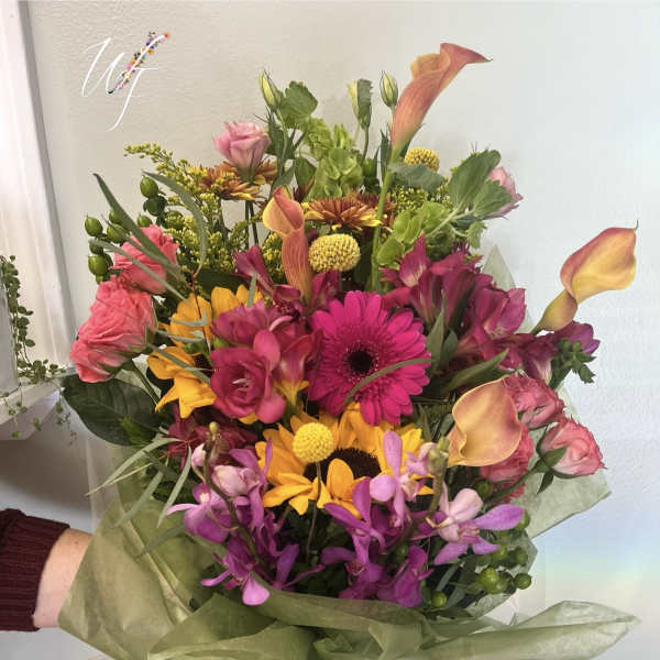 Mixed bouquet with pink, yellow, and orange flowers wrapped in green paper