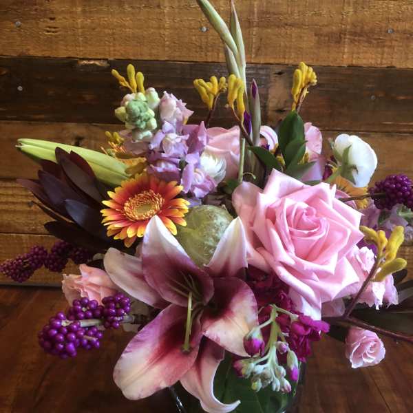 Pink roses and lilies in a glass vase with purple accents