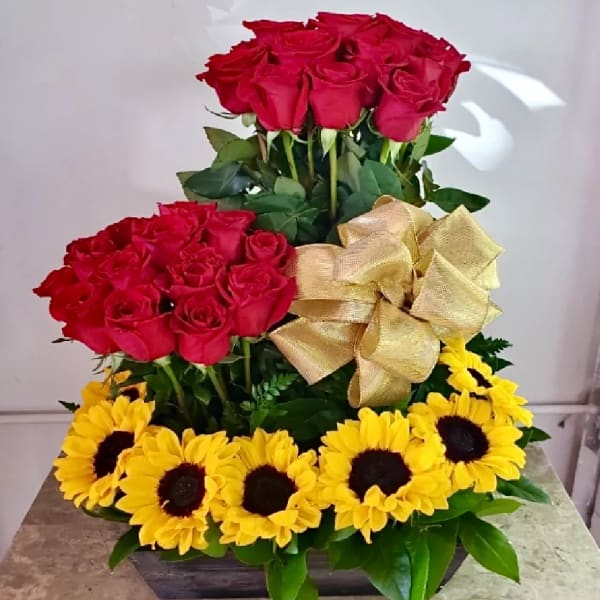 Tiered floral arrangement with red roses and yellow sunflowers in a low container