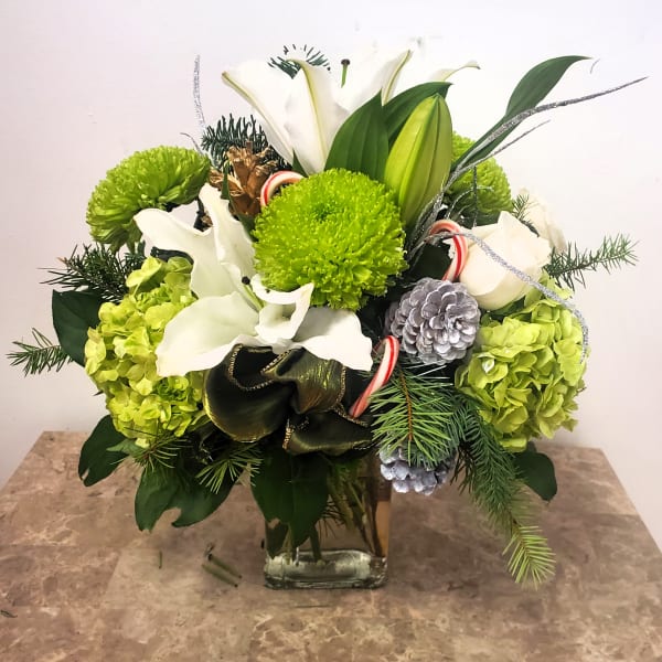 Holiday bouquet with white lilies, green mums, and pinecones in a glass vase