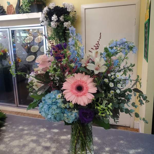 Mixed bouquet in a glass vase with pink gerbera, blue hydrangea, and white lilies