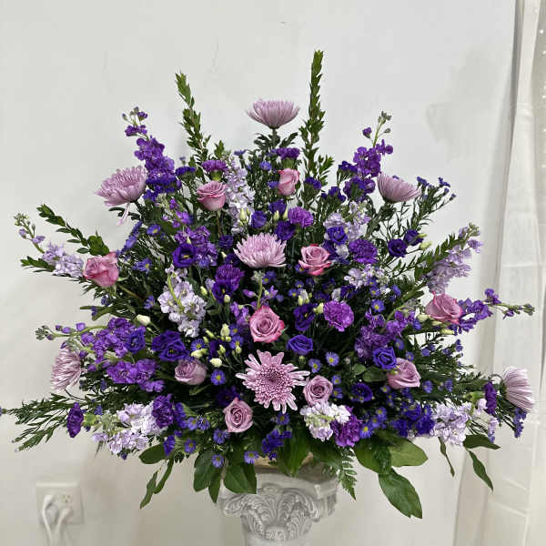 Large purple and pink floral arrangement in a decorative pedestal vase