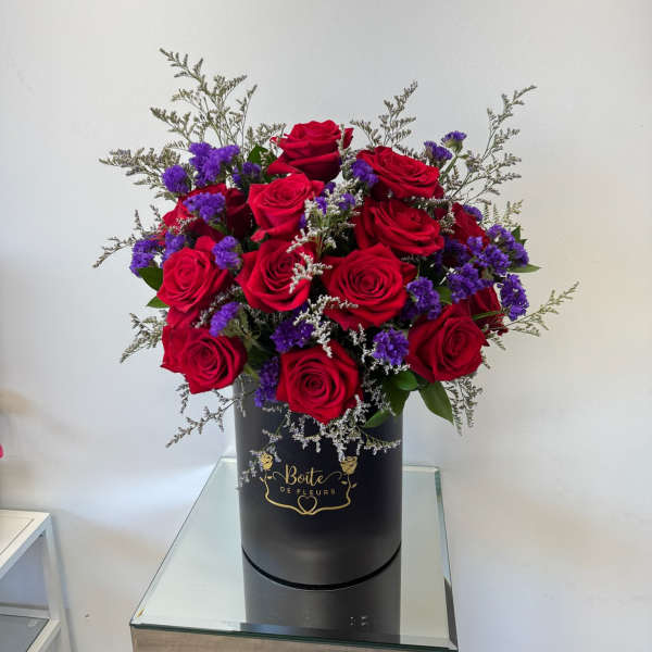 Red roses and purple filler flowers in a black hatbox