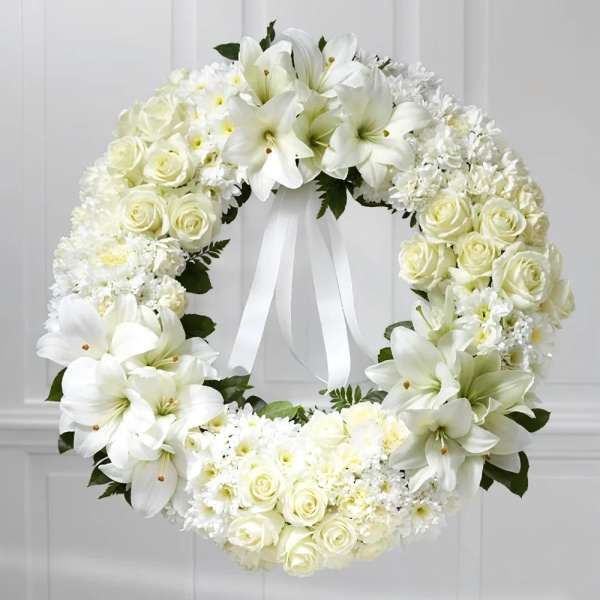 White floral wreath with roses and lilies tied with a ribbon