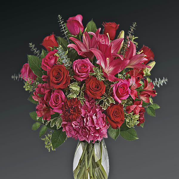 Bouquet of red and pink roses with lilies in a clear glass vase