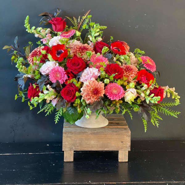 Large mixed bouquet of red, pink, and peach flowers in a white vase