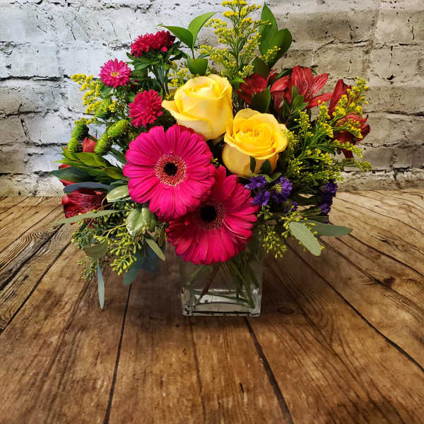 Bright mixed bouquet with yellow roses and pink gerbera daisies in a glass vase