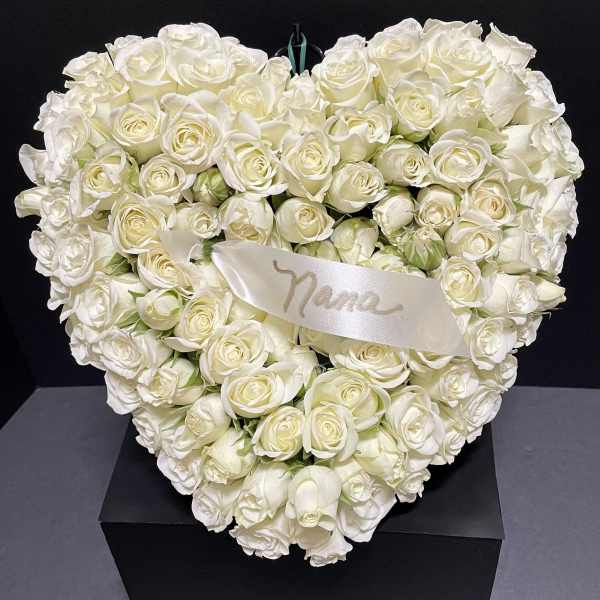 Heart-shaped arrangement of white roses with a satin ribbon on a black box